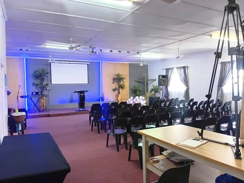 A functional assembly hall or clubhouse space featuring a raised stage, projector screen, and integrated track lighting, suitable for community gatherings or events.