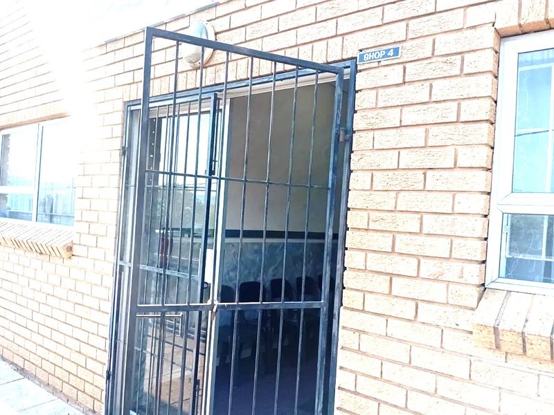 Front entrance of commercial shop unit featuring brick facade, aluminium window frames, and a security gate.