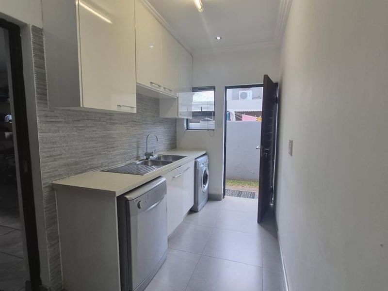 A functional scullery featuring modern white cabinetry, a stainless steel sink, tiled splashback, and direct access to the exterior.
