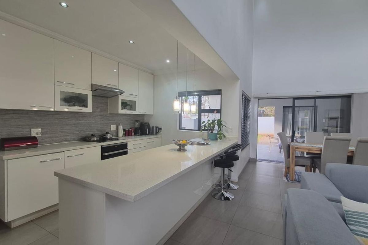 Modern open-plan kitchen featuring high-gloss cabinetry, stone countertops, and integrated appliances, flowing seamlessly into the living and dining area with access to the patio.