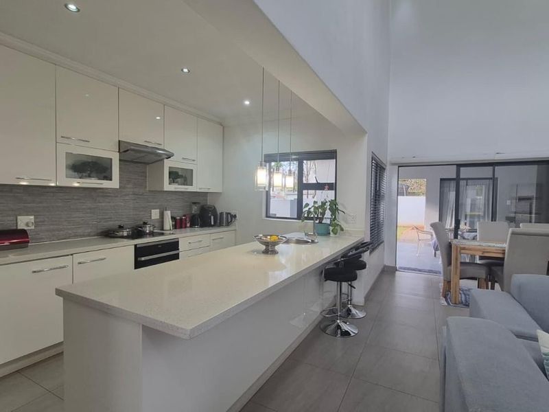 Modern open-plan kitchen featuring high-gloss cabinetry, stone countertops, and integrated appliances, flowing seamlessly into the living and dining area with access to the patio.