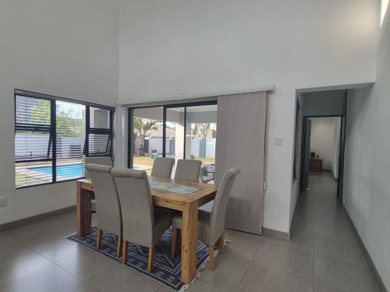 Spacious open-plan living and dining area featuring high ceilings, large windows, and sliding doors providing seamless access to the outdoor patio and pool area.