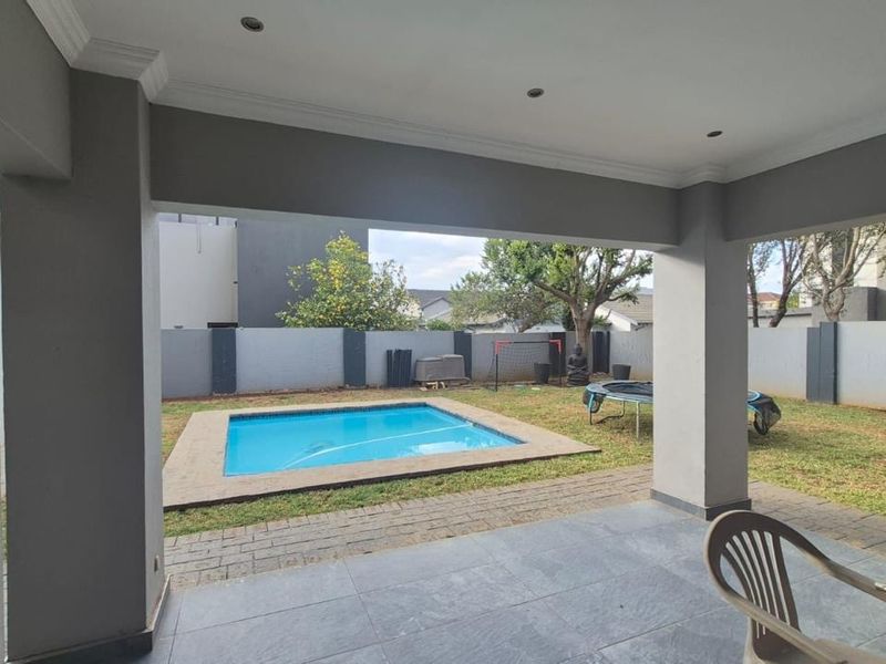 A covered patio area overlooking a private garden with a swimming pool and paved surround, featuring modern tiled flooring and recessed lighting.