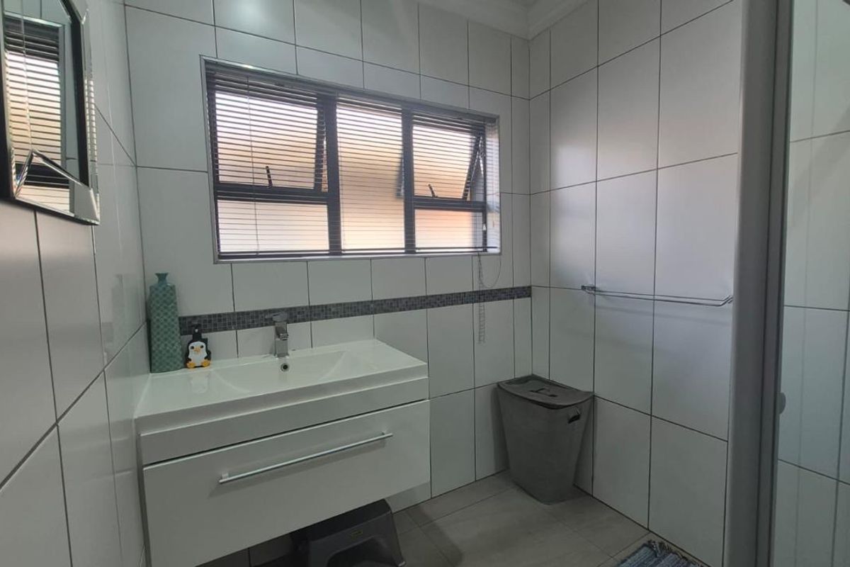 A clean, modern bathroom featuring a wall-mounted vanity with basin, tiled walls, and a glass-enclosed shower.