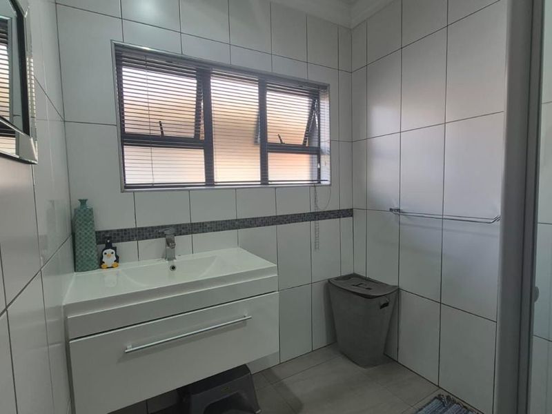 A clean, modern bathroom featuring a wall-mounted vanity with basin, tiled walls, and a glass-enclosed shower.