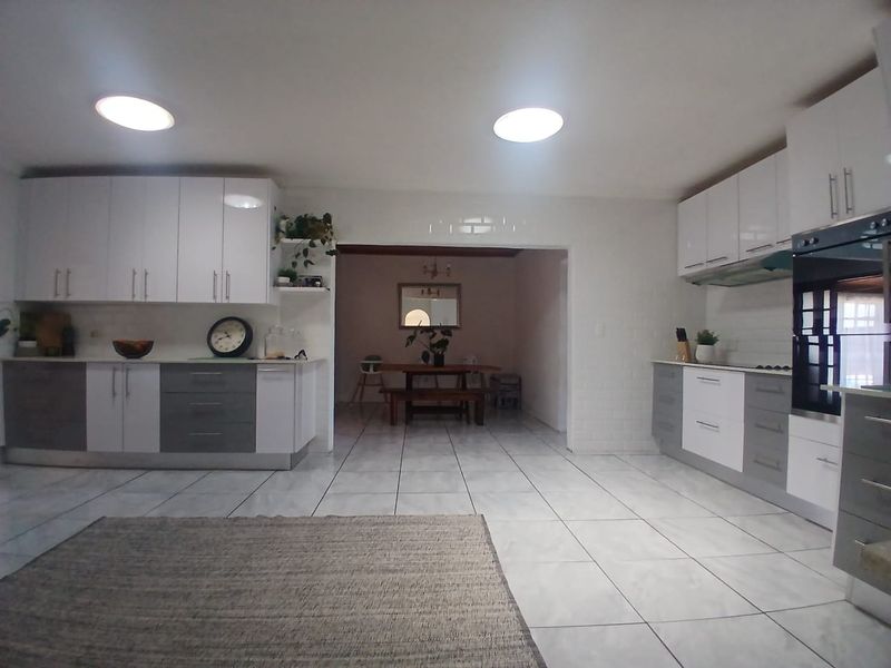 Spacious open-plan kitchen featuring modern two-tone cabinetry, tiled flooring, and integrated appliances, flowing seamlessly into the adjacent dining area.