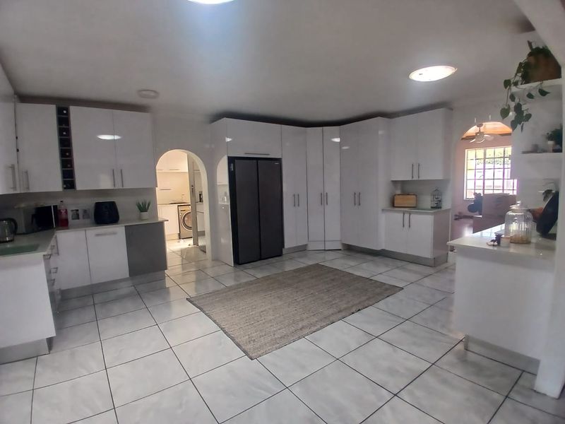 Modern kitchen featuring high-gloss white cabinetry, stone countertops, and tiled flooring, with an open-plan layout and an adjacent scullery area.