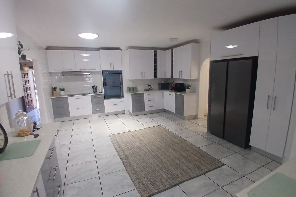 Modern kitchen featuring white and grey cabinetry, stone countertops, integrated oven, extractor fan, and tiled flooring with ample storage space.