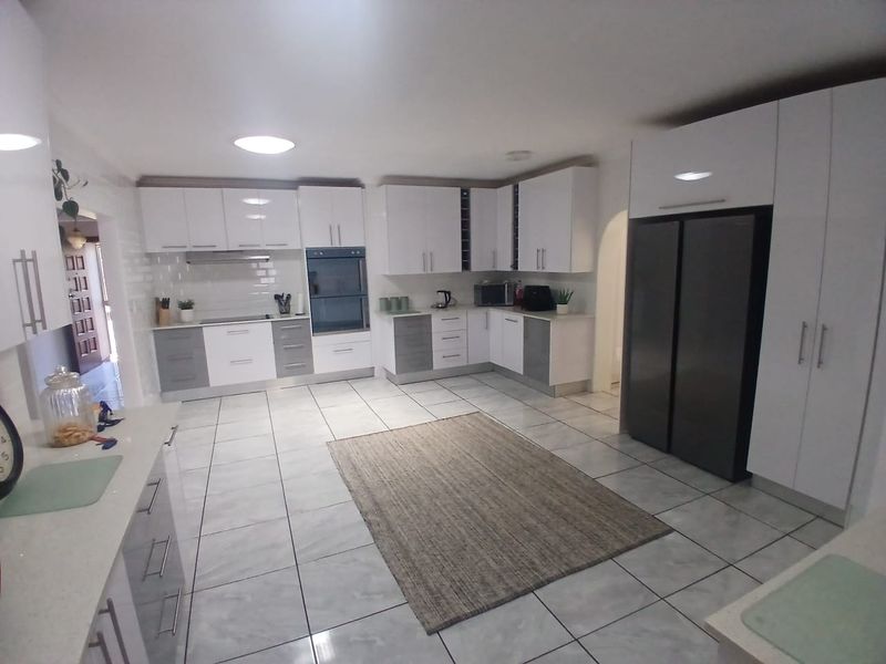 Modern kitchen featuring white and grey cabinetry, stone countertops, integrated oven, extractor fan, and tiled flooring with ample storage space.
