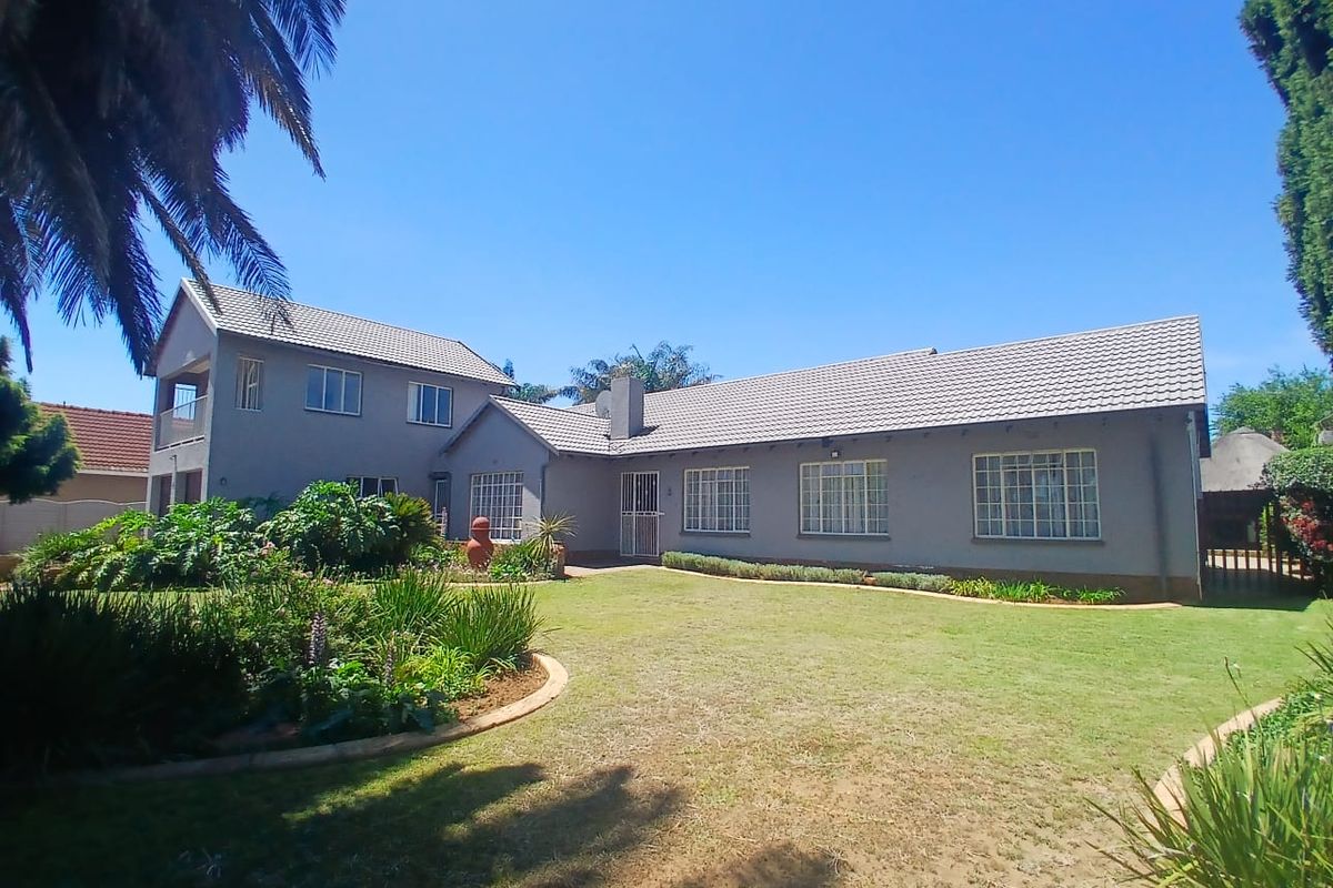 A view of the rear elevation of the house featuring a tiled roof, brick chimney, and a well-maintained garden with established landscaping.