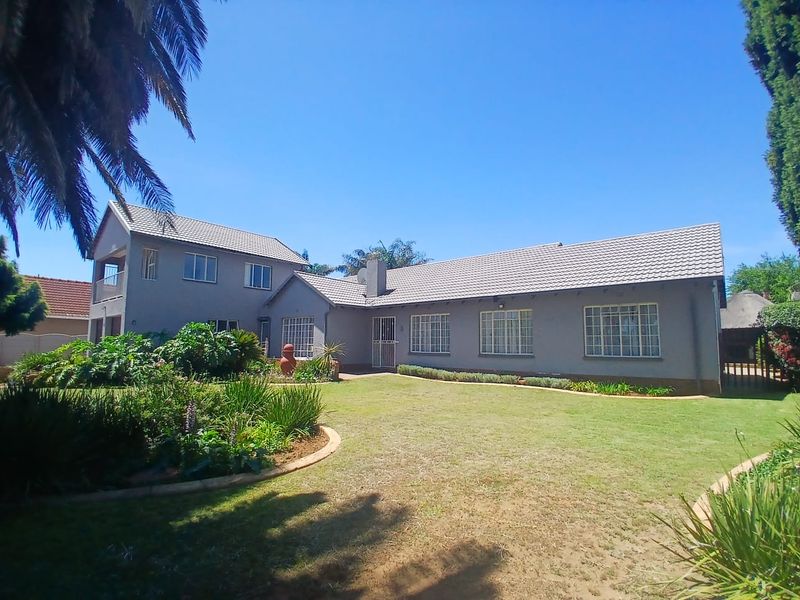 A view of the rear elevation of the house featuring a tiled roof, brick chimney, and a well-maintained garden with established landscaping.