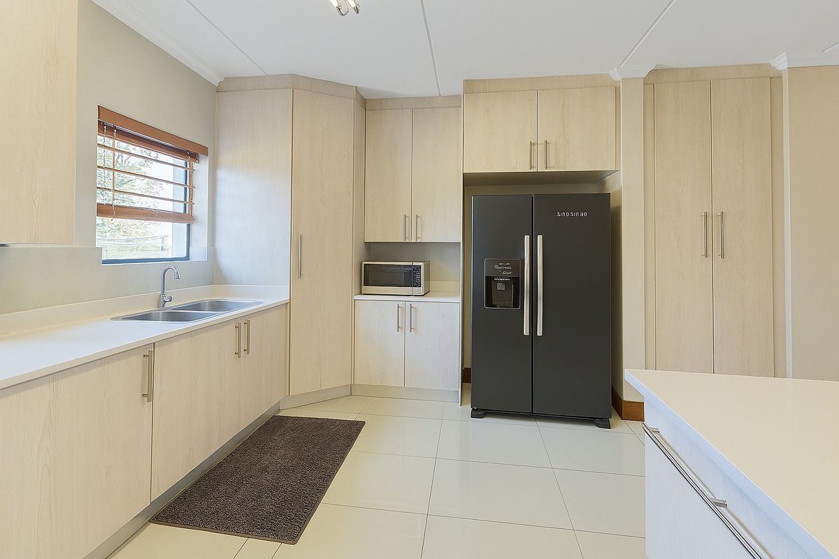 A modern, well-maintained kitchen featuring light wood-finish cabinetry, stone countertops, a double sink, and tiled flooring with ample storage space.