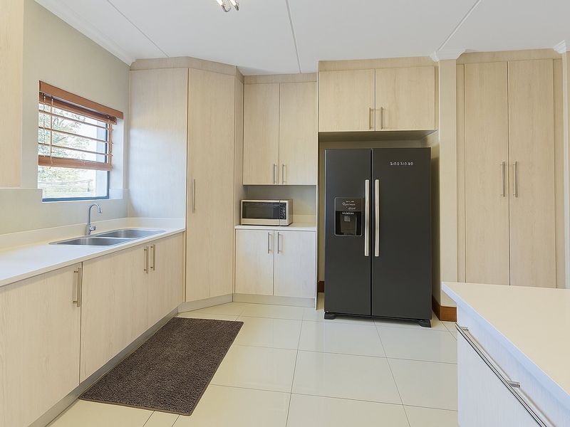 A modern, well-maintained kitchen featuring light wood-finish cabinetry, stone countertops, a double sink, and tiled flooring with ample storage space.