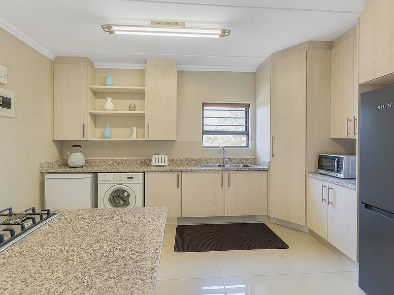 A well-maintained kitchen featuring light wood cabinetry, granite countertops, a built-in gas hob, and tiled flooring with integrated laundry and appliance space.