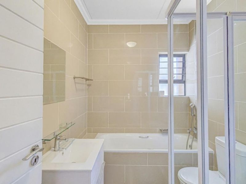 A clean and modern bathroom featuring a built-in vanity, bathtub, separate shower enclosure, and neutral wall tiling.
