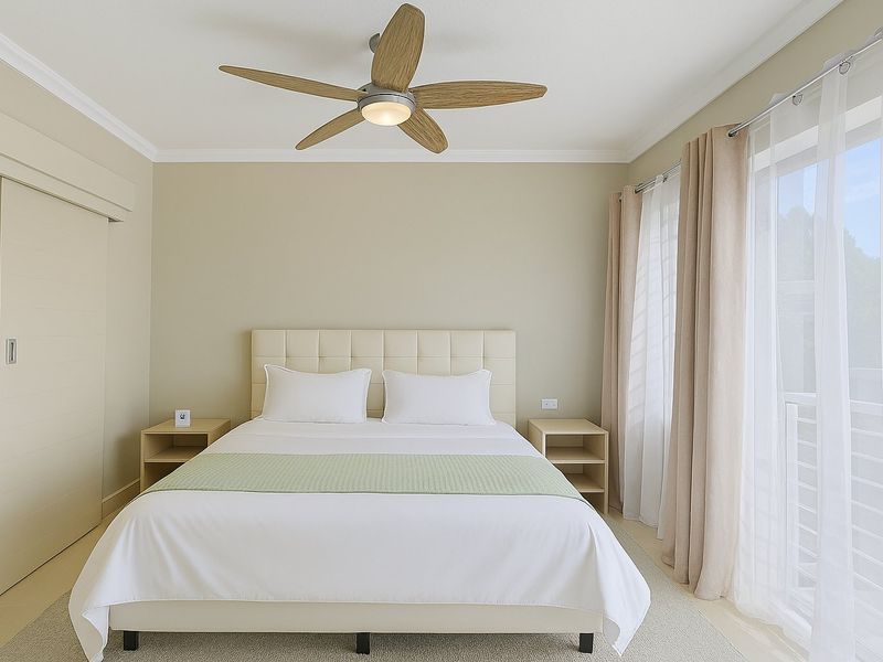 A well-maintained bedroom featuring a modern ceiling fan, neutral wall tones, and a sliding door providing access to an outdoor area.