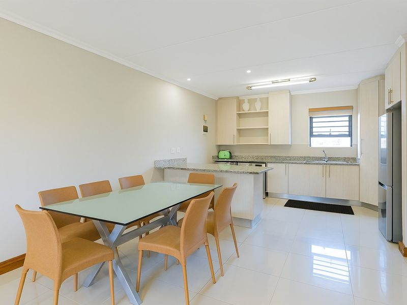 A bright open-plan kitchen and dining area featuring modern cabinetry, granite countertops, and polished tiled flooring, creating a functional and cohesive living space.