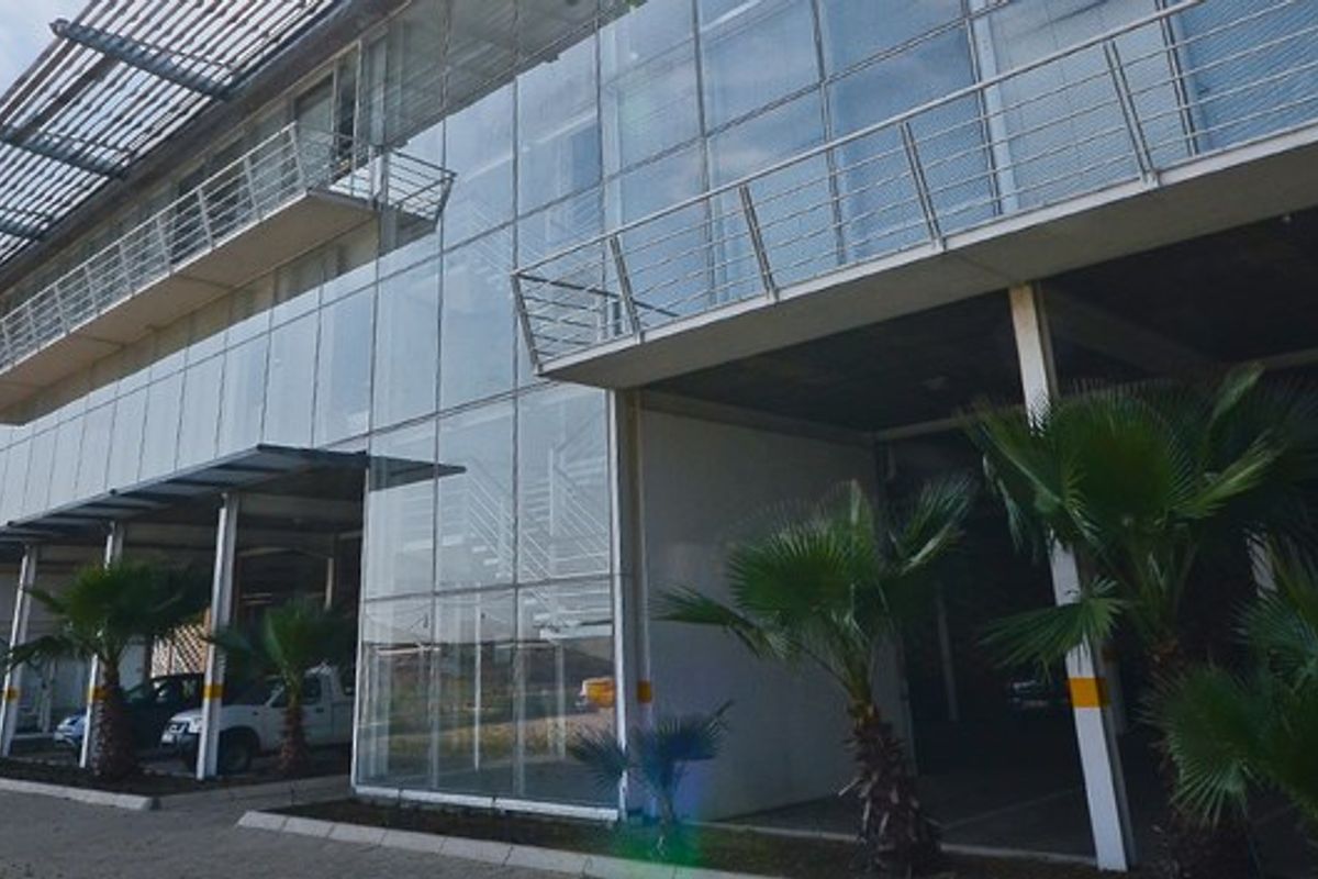 Modern industrial building facade featuring extensive glass curtain walling, steel balcony railings, and integrated covered parking bays.