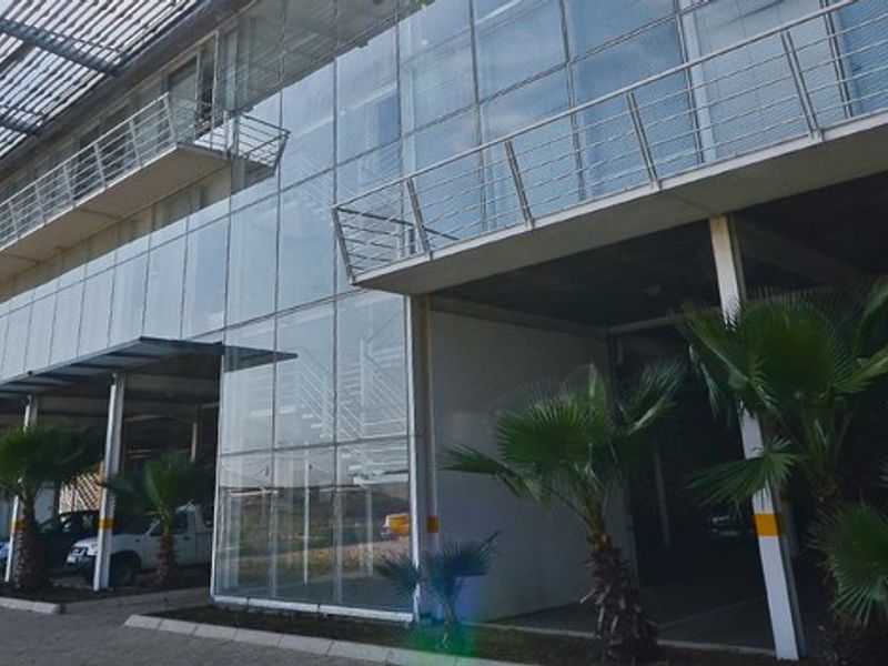 Modern industrial building facade featuring extensive glass curtain walling, steel balcony railings, and integrated covered parking bays.