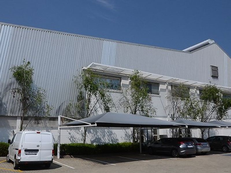 Exterior view of a large industrial warehouse facility featuring corrugated metal cladding and dedicated shaded parking bays.
