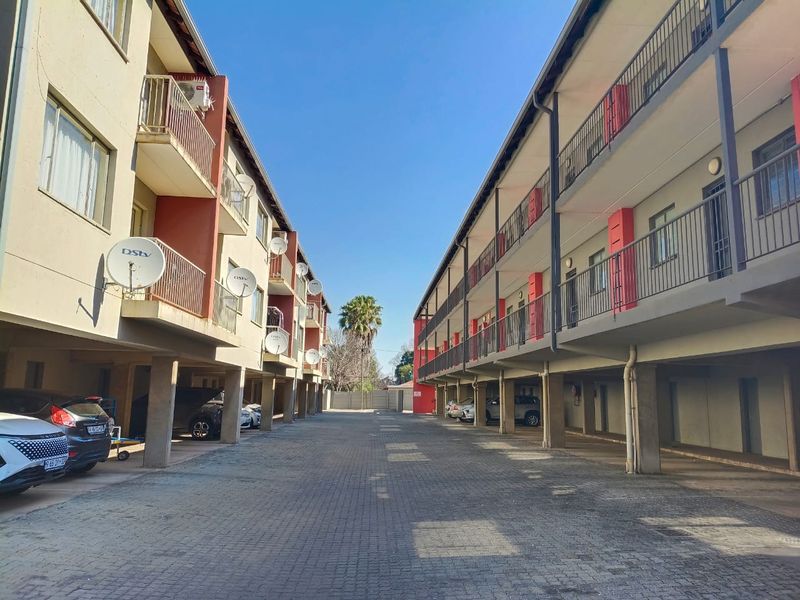 Exterior view of an apartment complex featuring paved driveway access, covered ground-level parking bays, and multi-story residential units with private balconies.
