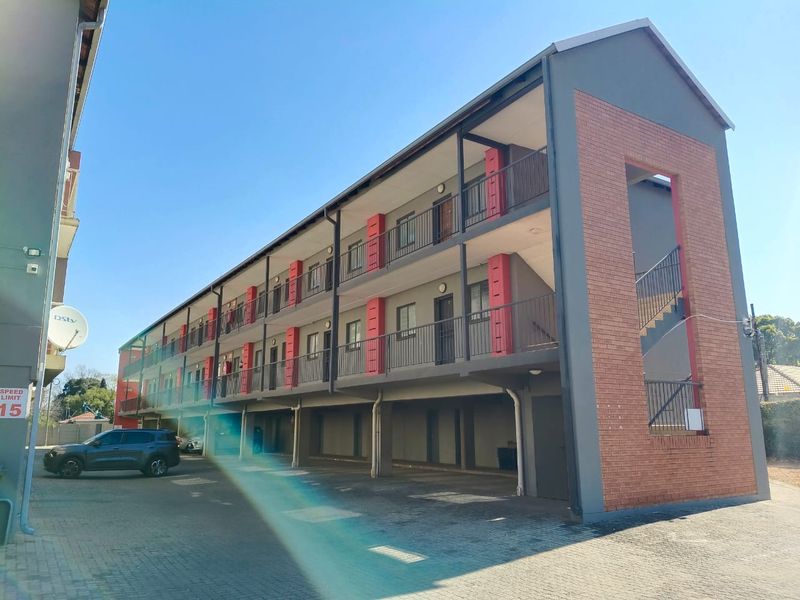 A multi-story apartment building featuring a modern facade with brick accents, external stairwell, and covered ground-level parking bays.