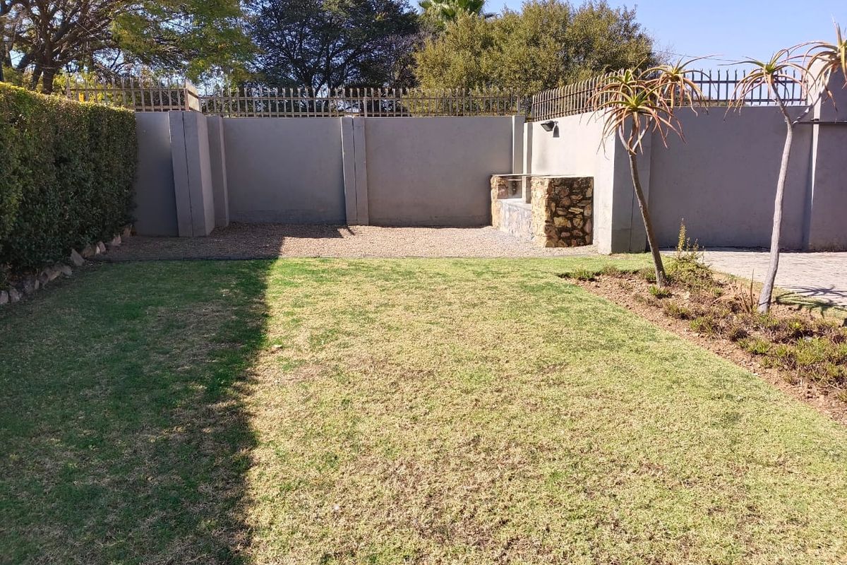 A private rear garden featuring a well-maintained lawn, perimeter wall with security spikes, and a built-in stone-clad braai area.