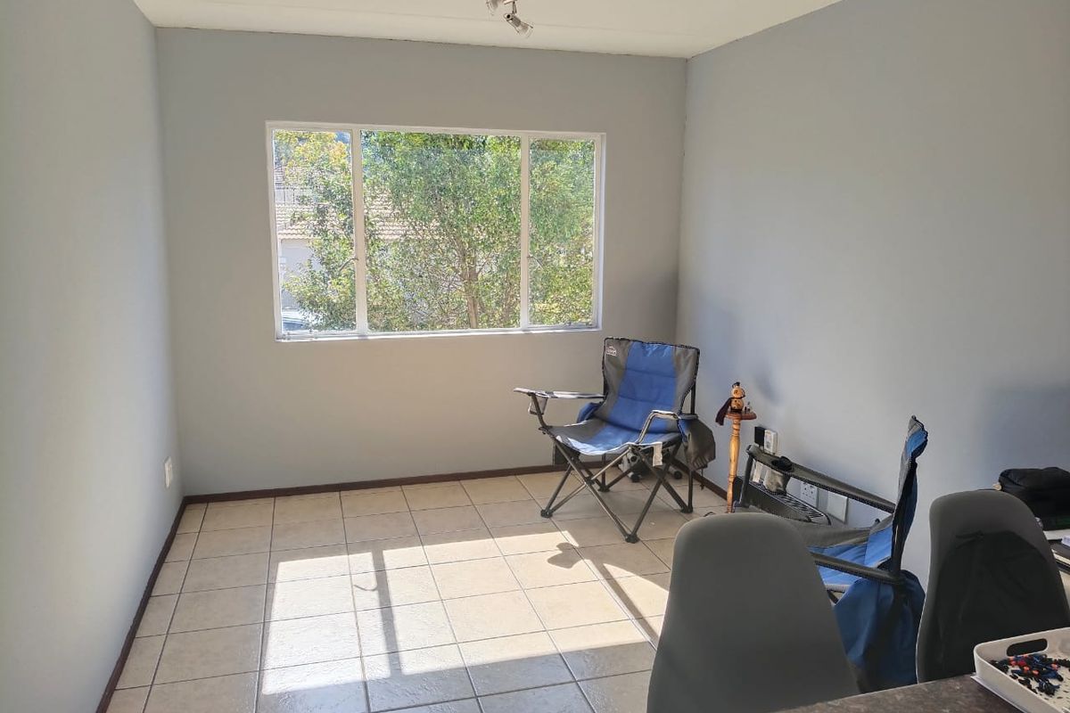 A bright, neutrally painted living area featuring tiled flooring and a large window, offering a clean and versatile space ready for personalization.