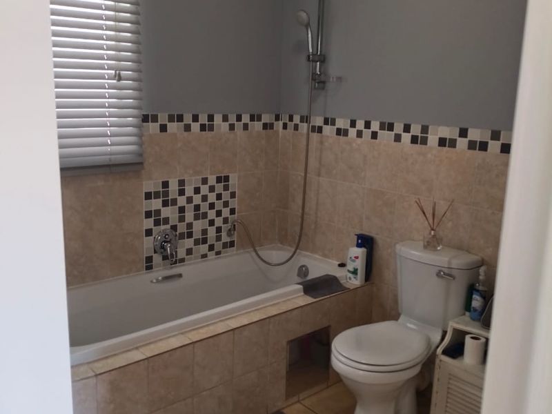 A functional bathroom featuring a bathtub with shower mixer, toilet, and neutral tiled finishes with a decorative mosaic border.