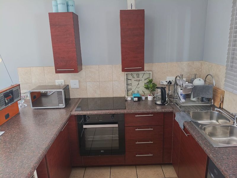 A functional kitchen featuring dark wood cabinetry, laminate countertops, a built-in oven with electric hob, and a double bowl stainless steel sink.