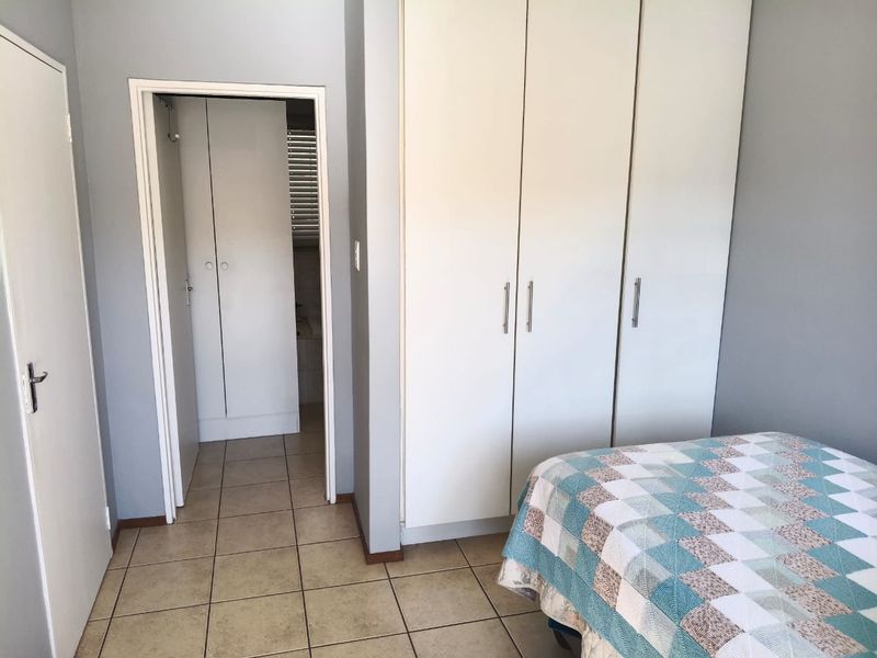 A bedroom featuring built-in cupboards, tiled flooring, and a doorway leading to an adjoining bathroom area.