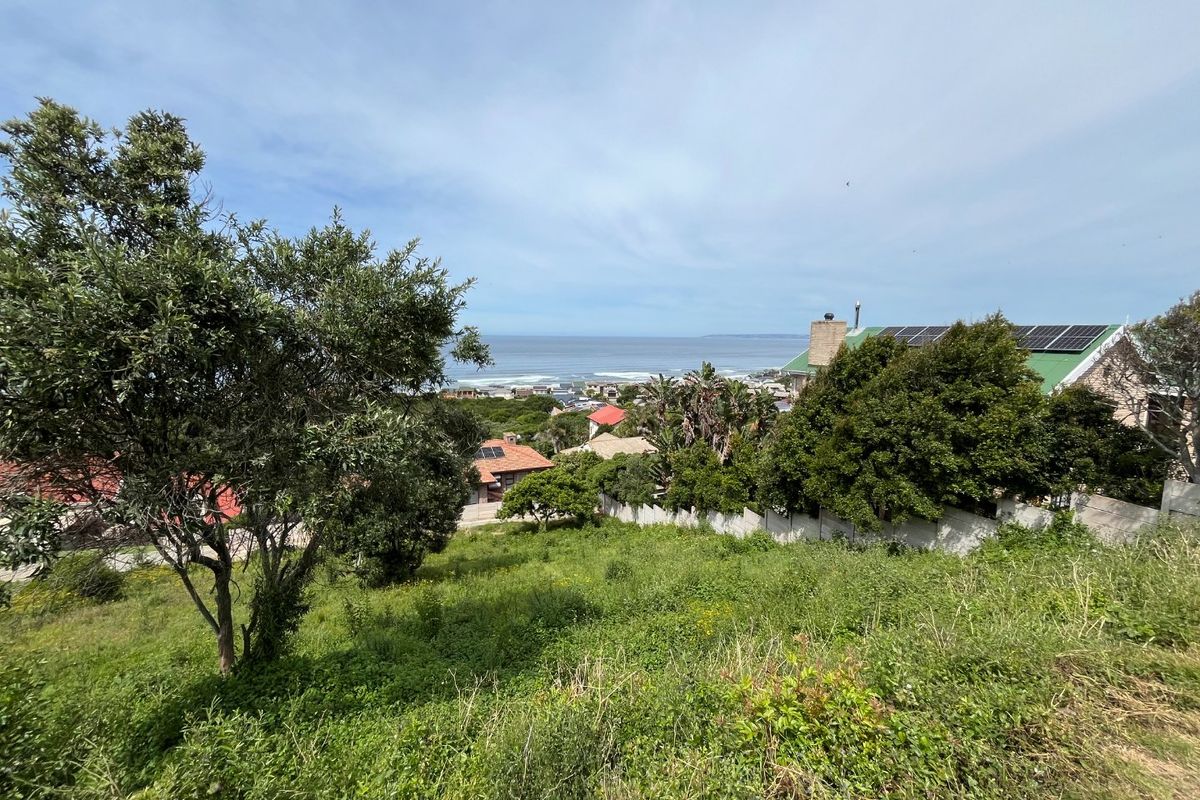 A scenic view overlooking a sloped residential plot with coastal and ocean vistas in the background.