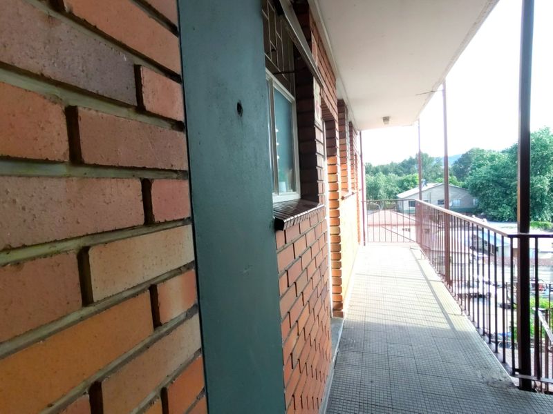 A covered exterior balcony featuring exposed brick walls, tiled flooring, and a metal safety railing overlooking the surrounding neighborhood.