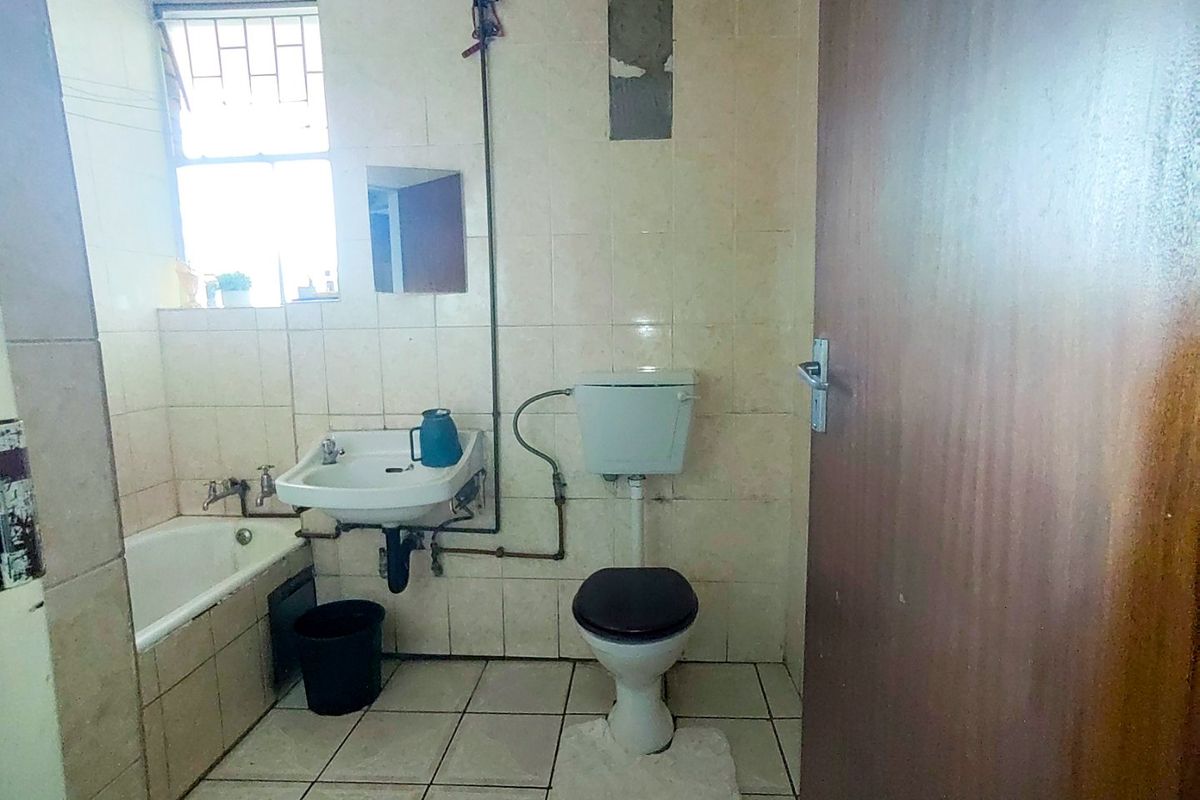 A dated bathroom featuring a bathtub, wall-mounted basin, and toilet, requiring renovation to update the finishes and address exposed plumbing.