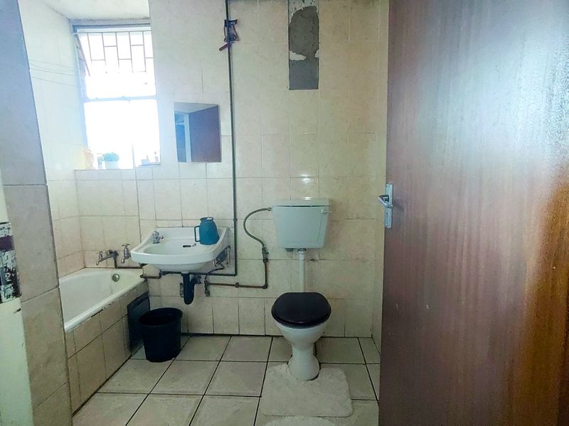 A dated bathroom featuring a bathtub, wall-mounted basin, and toilet, requiring renovation to update the finishes and address exposed plumbing.