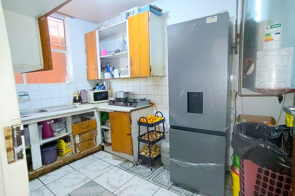 A compact kitchen featuring tiled flooring, a tiled backsplash, built-in cabinetry, and a gas hob, requiring significant cosmetic updates and maintenance.