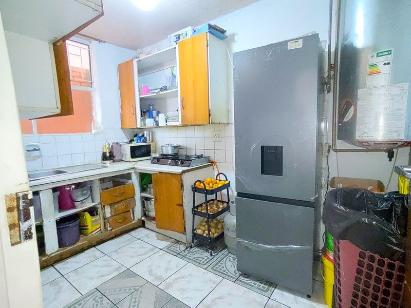 A compact kitchen featuring tiled flooring, a tiled backsplash, built-in cabinetry, and a gas hob, requiring significant cosmetic updates and maintenance.