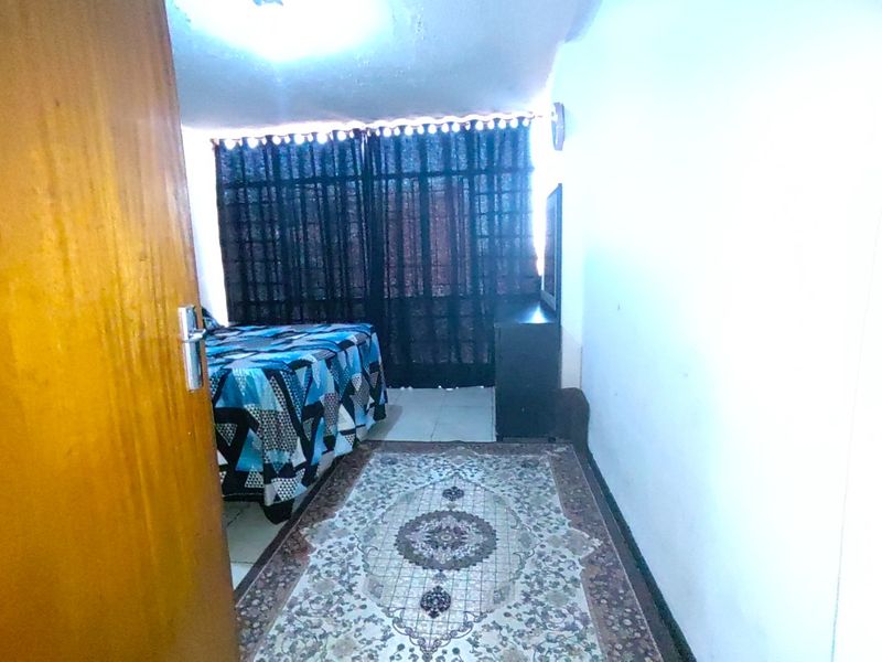 A bedroom featuring tiled flooring and access to a balcony through a sliding door, currently showing signs of wear on the ceiling and walls.