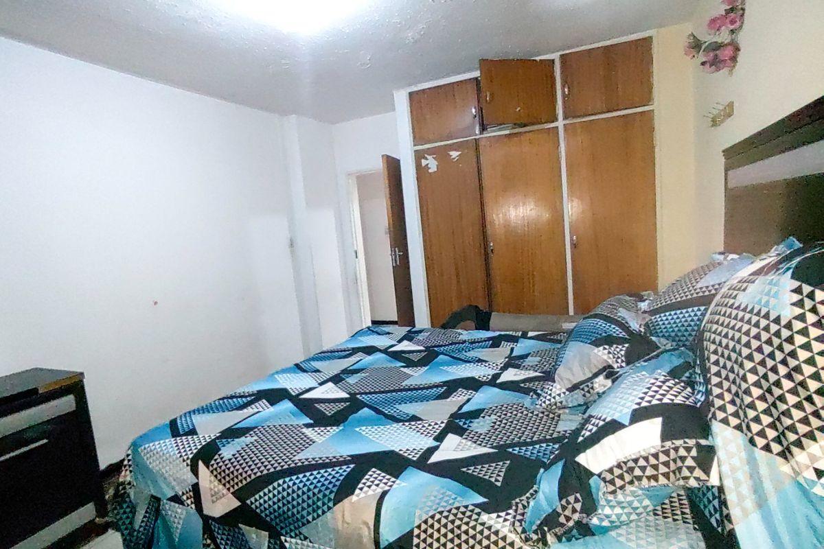 A bedroom featuring a built-in wooden wardrobe and overhead lighting, requiring cosmetic updates to the ceiling and finishes.