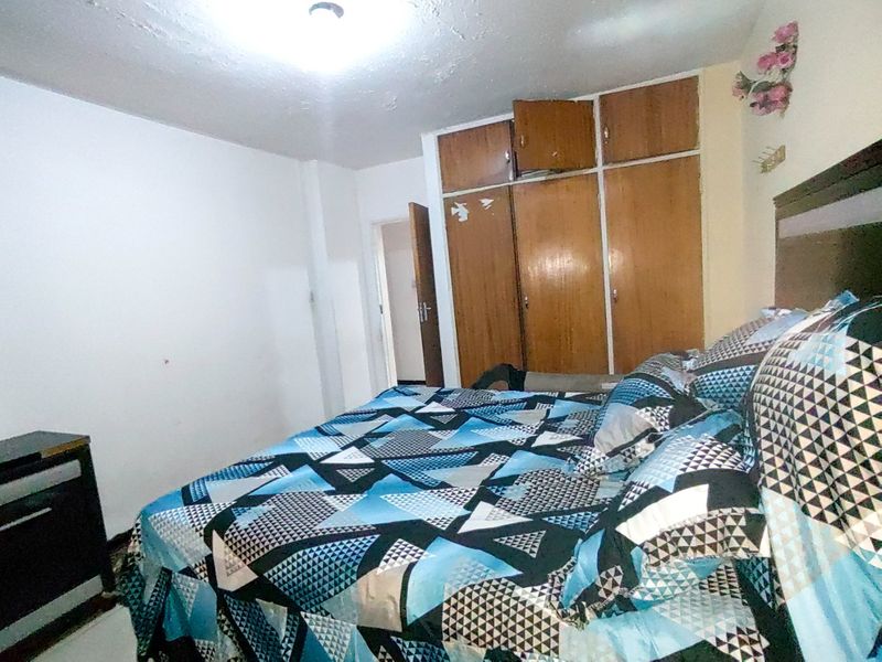 A bedroom featuring a built-in wooden wardrobe and overhead lighting, requiring cosmetic updates to the ceiling and finishes.
