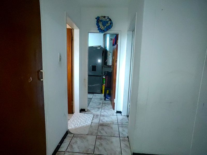 A narrow interior hallway featuring tiled flooring and access to adjacent rooms, showing signs of wear and requiring cosmetic updates.