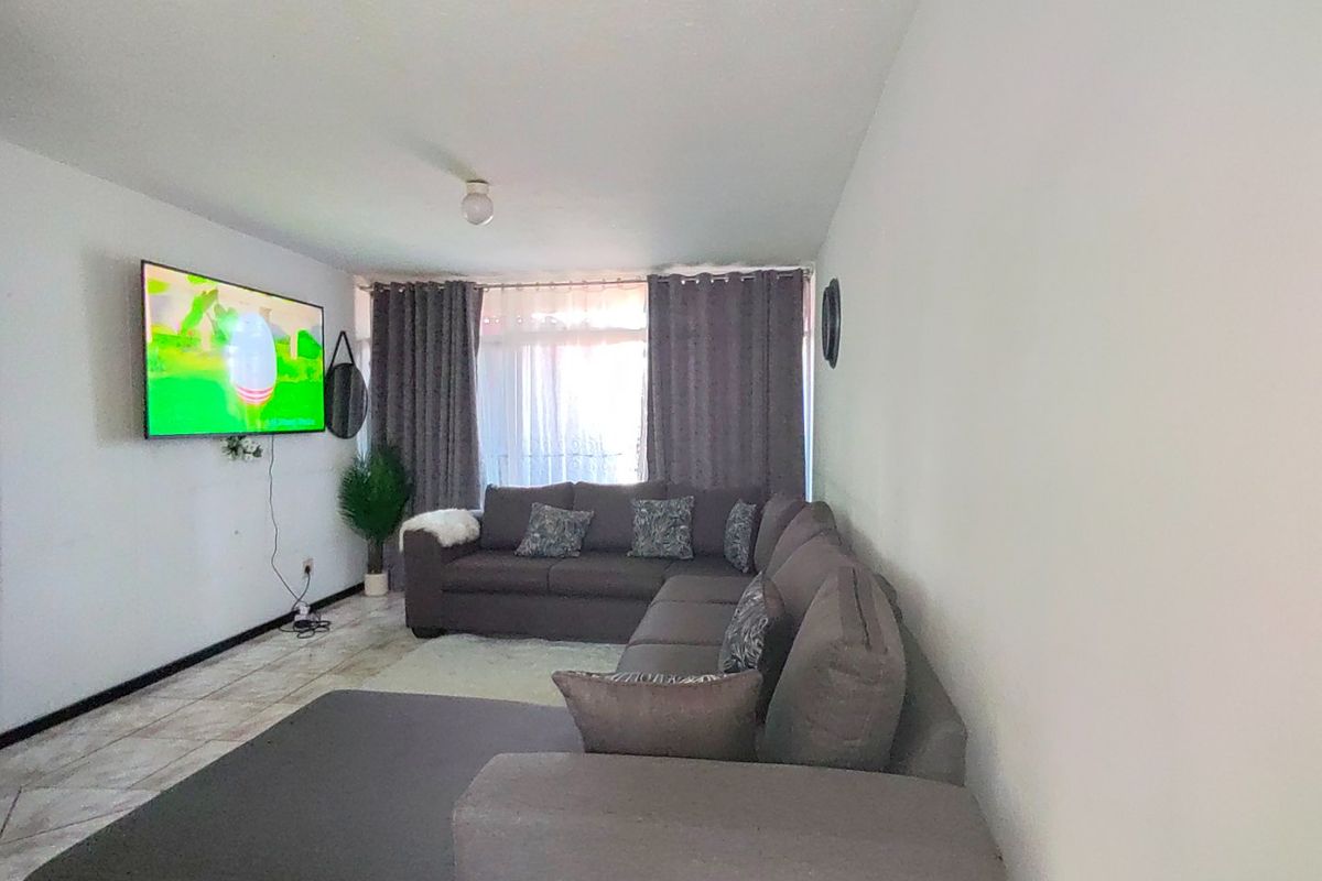 A functional living room featuring tiled flooring and large windows with curtains, providing a comfortable space for relaxation and entertainment.