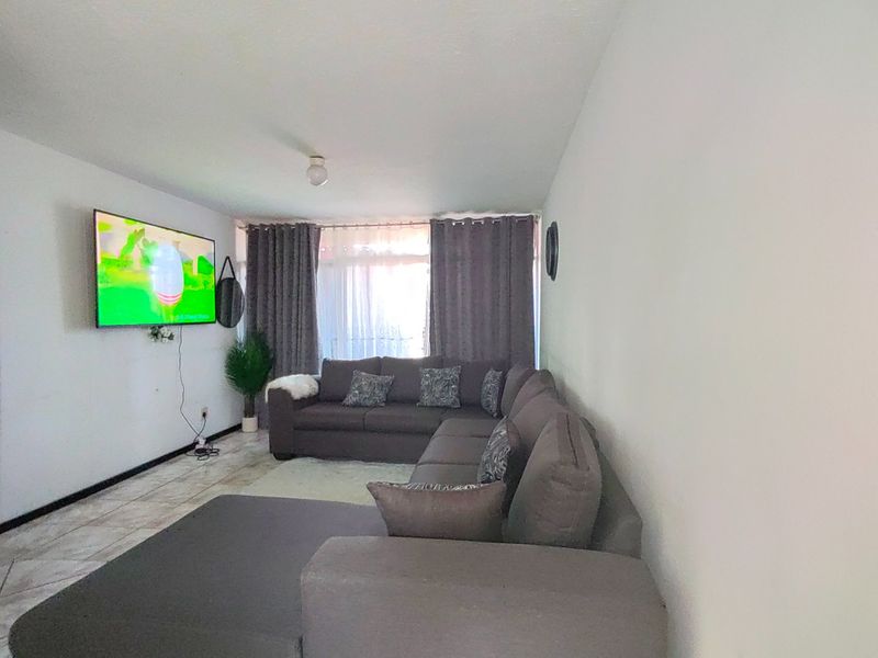 A functional living room featuring tiled flooring and large windows with curtains, providing a comfortable space for relaxation and entertainment.