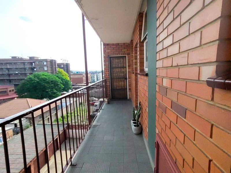 A functional balcony featuring tiled flooring, a metal balustrade, and brick exterior walls, offering an elevated view of the surrounding urban area.