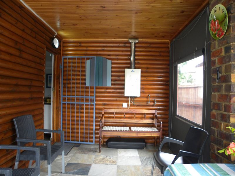 Covered patio area featuring rustic timber log walls, tongue and groove ceiling, slate tile flooring, and a wall-mounted gas geyser.