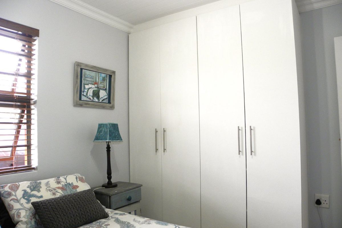 A well-maintained bedroom featuring floor-to-ceiling built-in cupboards, crown molding, and timber venetian blinds, offering a clean and functional living space.