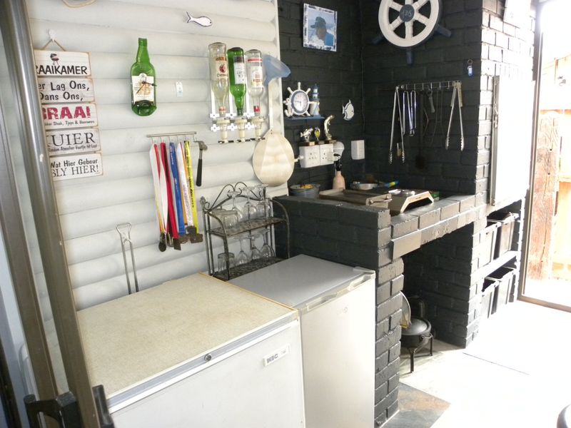Covered patio area featuring a built-in brick braai and fireplace, providing a functional outdoor entertainment space.