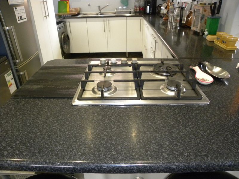 A functional kitchen featuring a central gas hob, dark granite countertops, and ample white cabinetry with an integrated washing machine.
