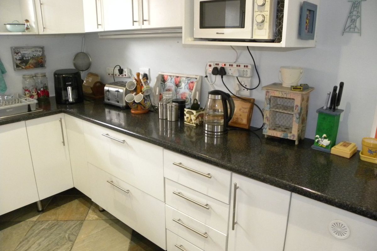 A functional kitchen featuring white cabinetry, dark laminate countertops, and tiled flooring, providing ample storage and workspace for daily meal preparation.