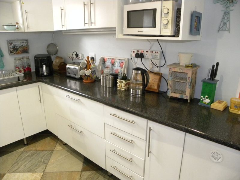 A functional kitchen featuring white cabinetry, dark laminate countertops, and tiled flooring, providing ample storage and workspace for daily meal preparation.